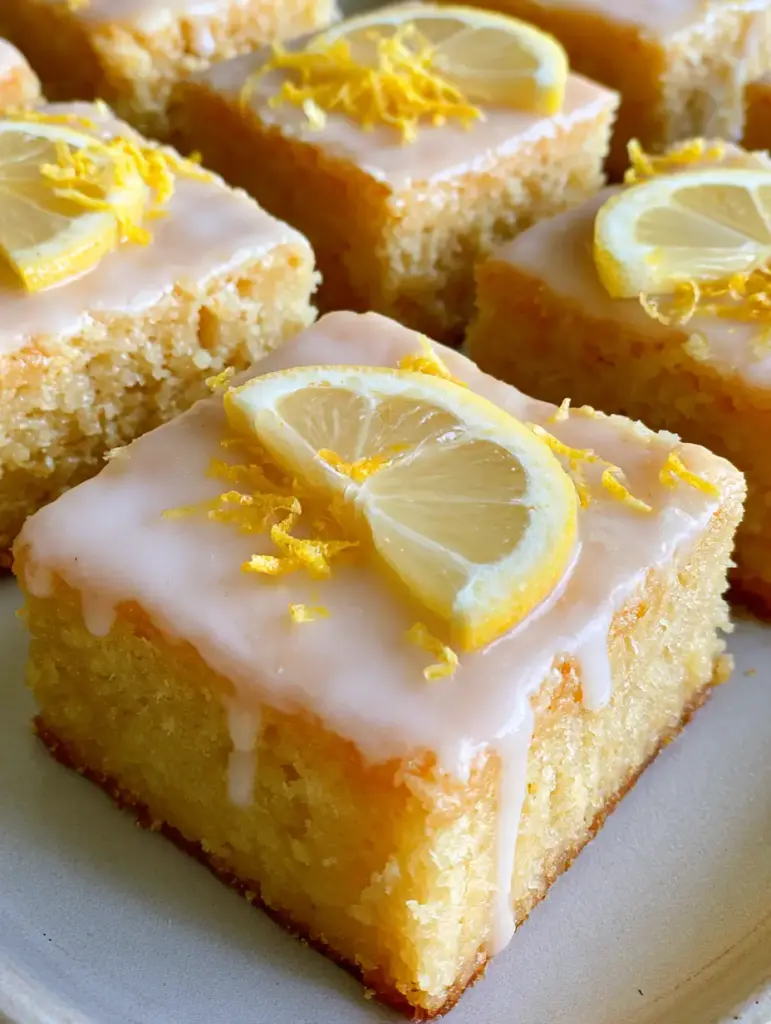 A stack of Lemon Blondies featuring a translucent glaze dripping down the sides and bright yellow zest curls.