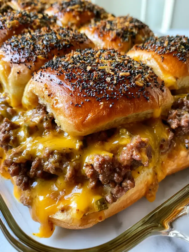 Close-up of golden-brown Hawaiian rolls packed in a glass dish, glazed with butter and poppy seeds. (White Trash Sliders)