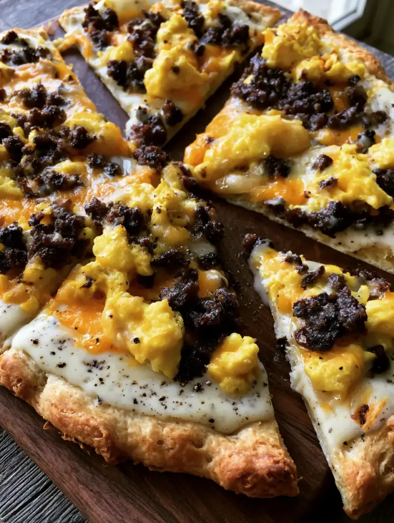 Sausage Gravy Breakfast Pizza with Flaky Biscuit Crust 2 Slightly overhead shot of Sausage Gravy Breakfast Pizza wedges with soft scrambled eggs and browned sausage on a rustic wooden board.